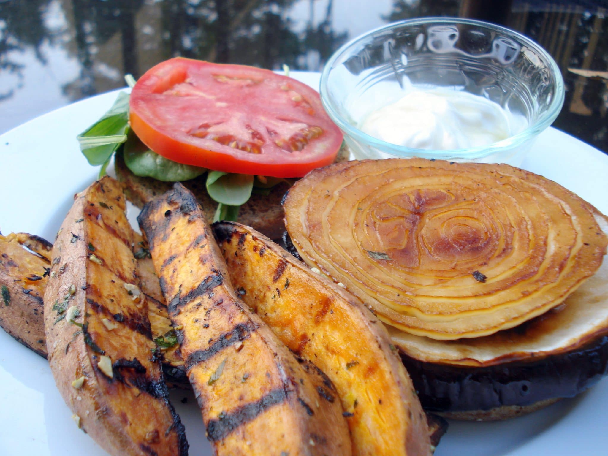 Grilled Onion and Eggplant Sandwich on a plate with grilled fries, tomato, and baby spinach